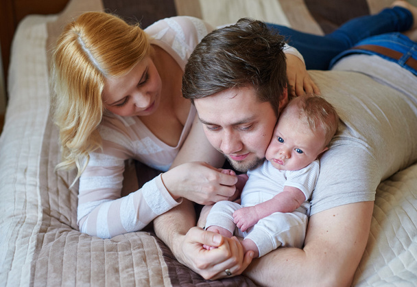 Beautiful happy couple and their baby relaxing in a bed together - Photo, Image