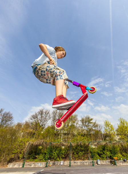 boy is jumping with a scooter over a spine in the skate park - Photo, Image