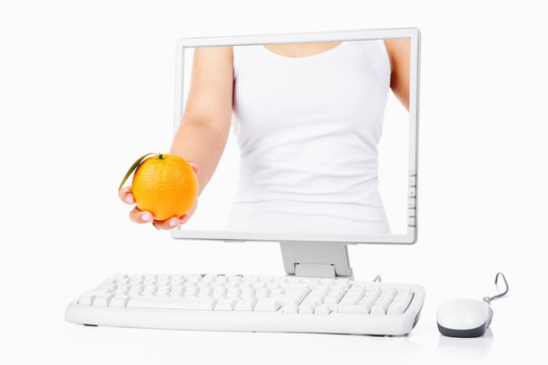 Female hand holding orange coming out from computer screen - Valokuva, kuva