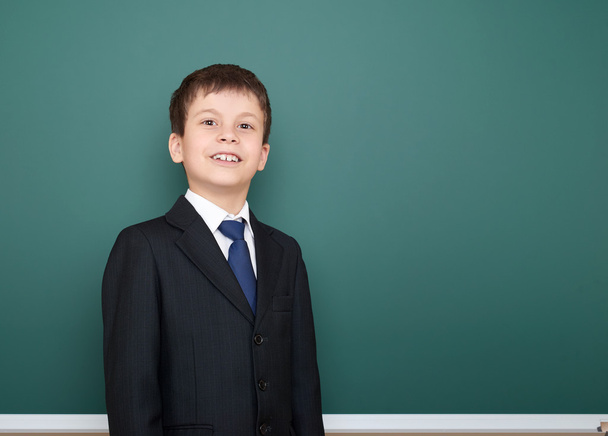 happy successfull school boy in black suit portrait on green chalkboard background, education concept - Valokuva, kuva