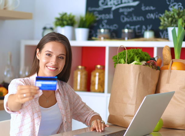 Smiling woman online shopping using tablet and credit card in kitchen - Foto, Imagen