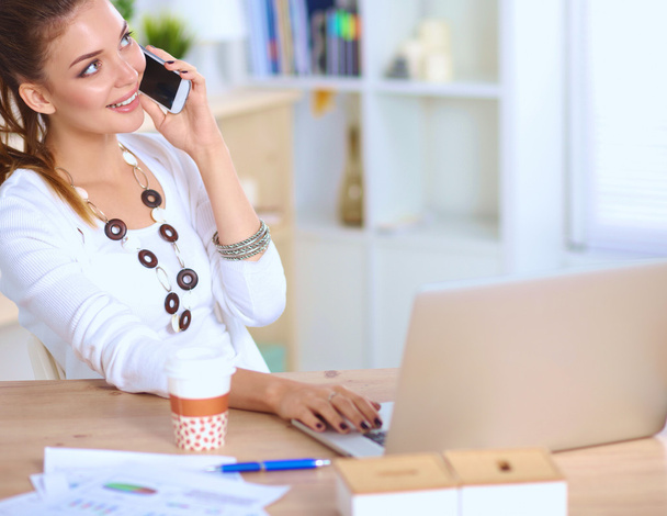 Young businesswoman sitting at the desk and talking on phone - Photo, Image