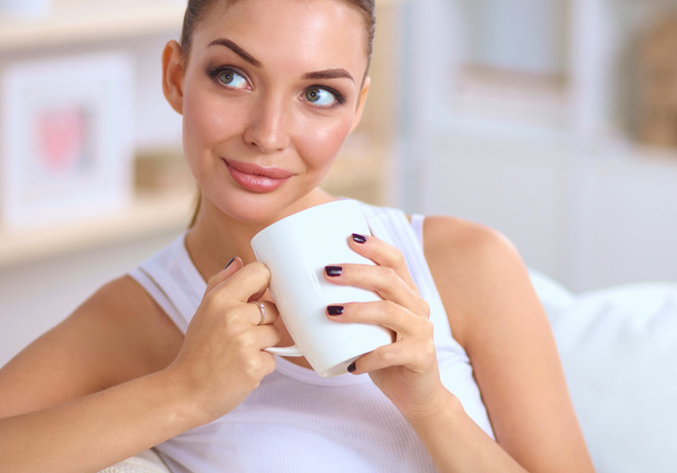 Young beautiful woman with a cup on sofa at home - Photo, Image