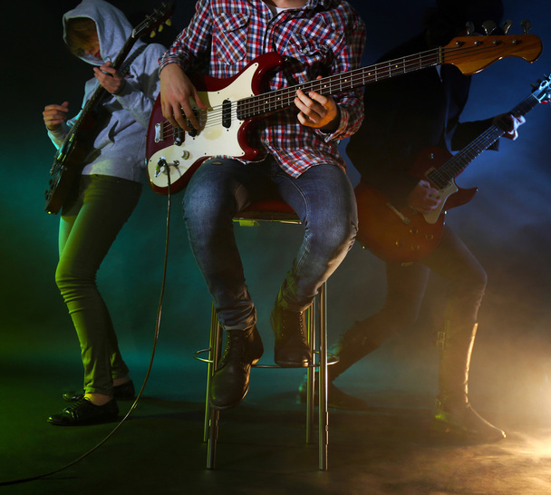 Молода група грає на електричній гітарі на освітленому туманному фоні
 - Фото, зображення