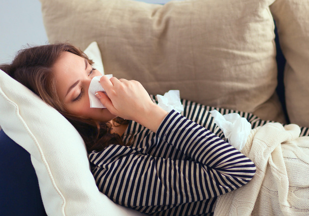 Προσωπογραφία γυναίκας άρρωστος φυσώντας τη μύτη της, ενώ κάθεται στον καναπέ - Φωτογραφία, εικόνα