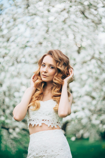 Spring beautiful girl, blonde, standing in a blooming Apple orchard . - 写真・画像