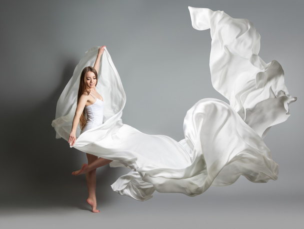 beautiful young girl dancing. The girl in flying white dress. A white cloth is flying in the air. White light dress - Фото, изображение