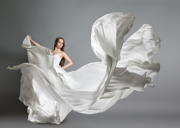 beautiful young girl dancing. The girl in flying white dress. A white cloth is flying in the air. White light dress - Foto, afbeelding