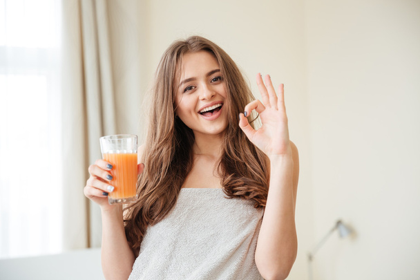 Woman holding glass with orange juice and showing thumb up - Foto, afbeelding