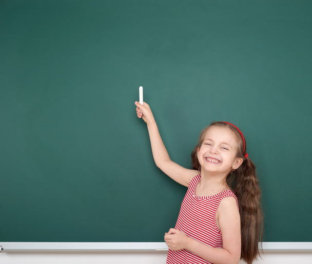 schoolgirl child in red striped dress point and drawing on green chalkboard background, summer school vacation concept - Fotoğraf, Görsel
