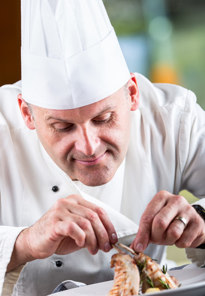Chef. Chef cooking.Chef decorating dish. Chef preparing a meal. Chef in hotel or restaurant kitchen prepares decorating dish with tweezers. Chef cooking, only hands. Decorate the rabbit thighs legs - Φωτογραφία, εικόνα