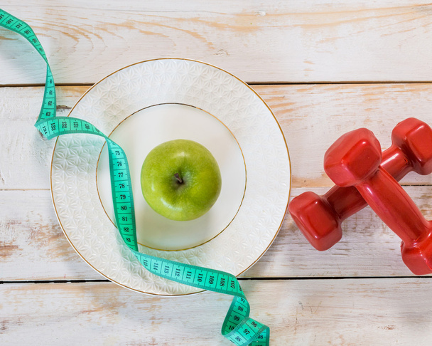 red dumbbells, measuring tape and apple - Foto, afbeelding