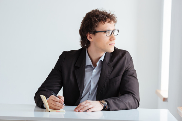 Pensive businessman writing something in notebook - Fotó, kép