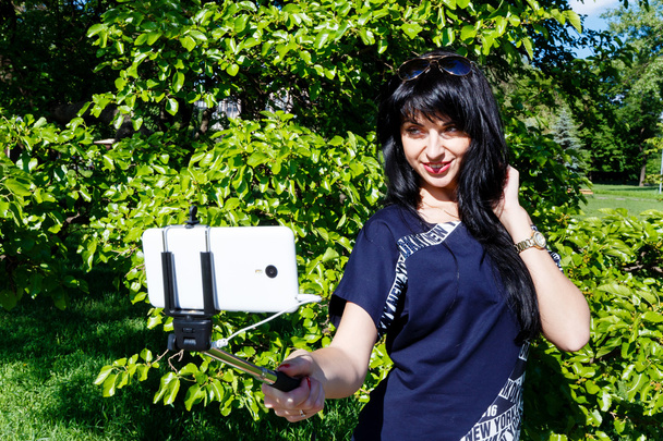 Mosolygó lány teszi selfie fotók segítségével a telefon és a monopod  - Fotó, kép