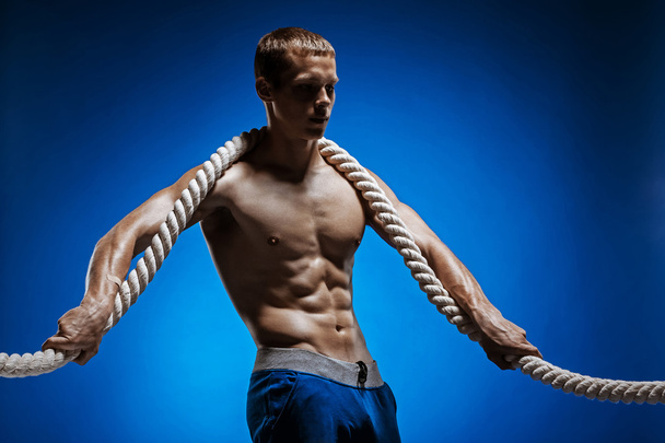 Fit young man with beautiful torso and a rope on blue background - Fotó, kép