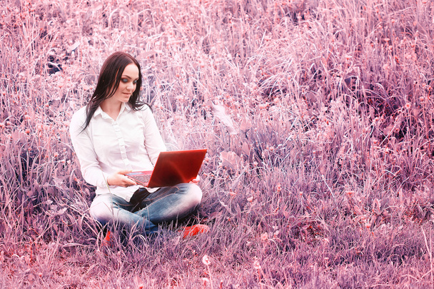 Fiatal nő ül a fűben, egy laptop előtt - Fotó, kép