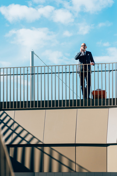 businessman leaning on handrail talking on smartphone - Foto, Imagen