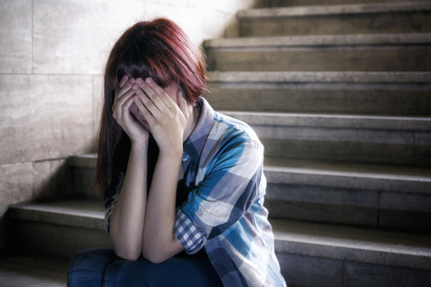 Депрессивная девочка в подростковом кризисе, сидя на ступеньках подвала, закрывает лицо руками. Сверху проникает естественный свет
. - Фото, изображение