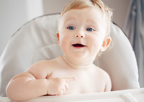 Close-up portret van schattig schattig grappig blond Kaukasisch lachende lachen baby jongen meisje met blauwe ogen zittend in hoge stoel op zoek weg glimlachend lachen - Foto, afbeelding