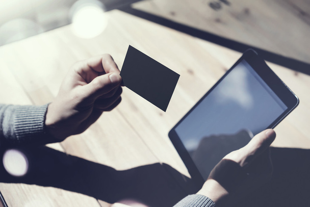 Photo Man Showing Blank Black Business Card, Holding Hand Modern Digital Tablet.Wood table Blurred Background.Mockup Ready  Private Information.Sunlight Reflections Screen Gadget.Horizontal mock up. - Fotó, kép