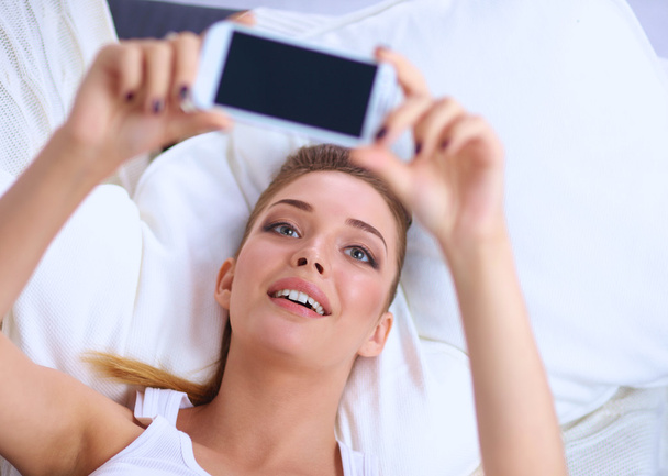 Happy brunette taking a photo of herself with her mobile phone in  bedroom - Zdjęcie, obraz