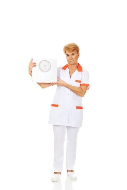 Smile elderly female doctor or nurse holds weigh scale - Photo, Image