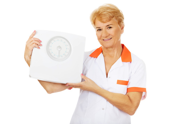 Smile elderly female doctor or nurse holds weigh scale - 写真・画像