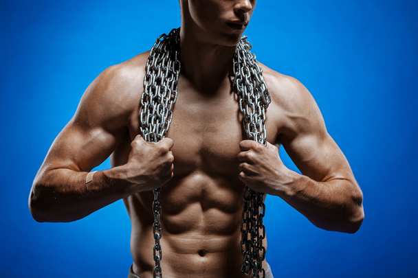 Muscular guy with chains on his shoulders against a blue wall - Fotografie, Obrázek