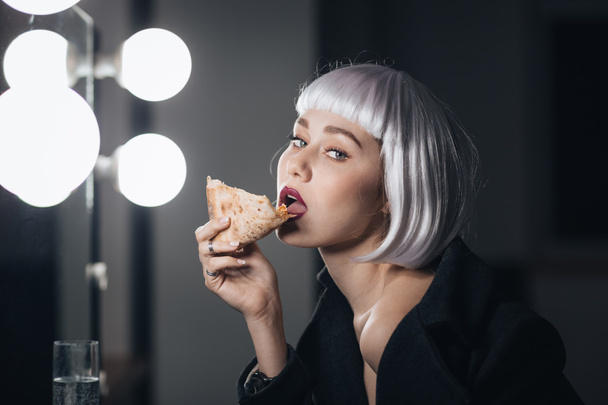 Tempting woman in blonde wig eating pizza and drinking champagne  - Fotó, kép