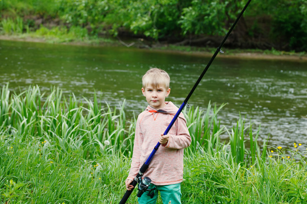 彼の手で釣り竿と川の近くのかわいい小さな男の子スタンド. - 写真・画像