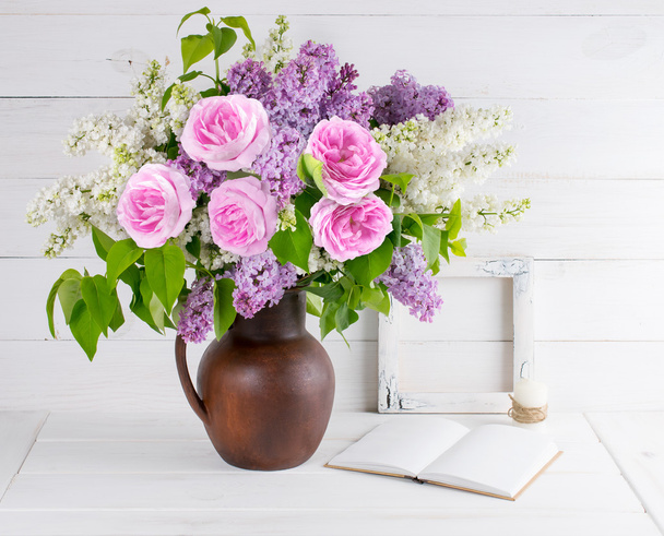 Lilac bouquet and roses in clay jug with open book and candle in - Fotó, kép