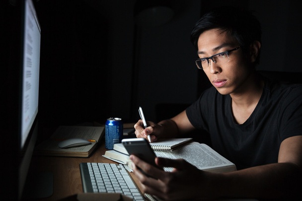 Man using smartphone while studying in the evening at home - Foto, Bild