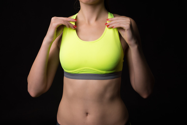 Un primer plano de una mujer deportiva con un estómago muscular usando deportes tocando con las manos sujetador amarillo neón
. - Foto, imagen