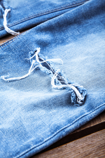 Ripped denim jeans on wooden background. Fashion, clothing, style, lifestyle - Foto, imagen