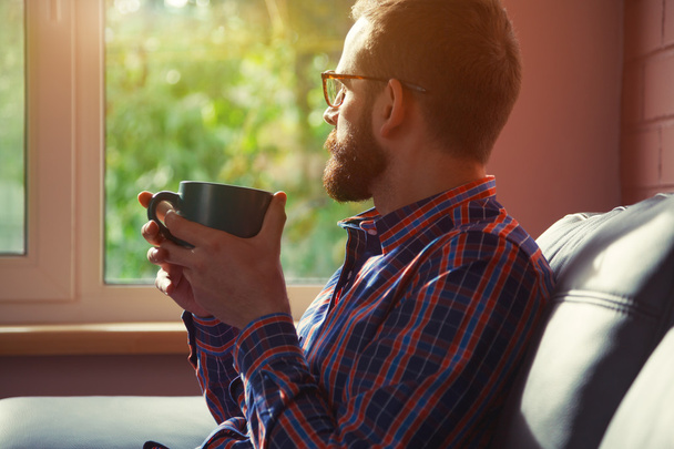 bearded man sitting with cup of morning coffee or tea and lookin - Photo, Image