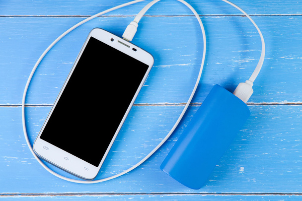 Smartphone und Backup-Akku auf blauem Holzhintergrund. - Foto, Bild