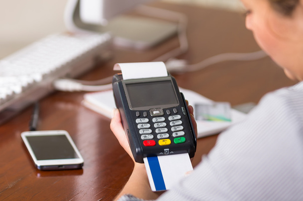 eine Frau, die mit einer weißen und blauen Kreditkarte bezahlen will, Karte in einem Automaten. auf einem Tisch ein Handy und ein Computer - Foto, Bild