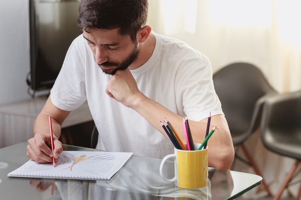 Portrait of a man sitting at a table coloring an adult coloring  - Foto, imagen