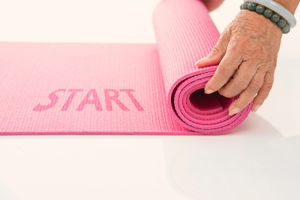 Senior hand's rolling pink yoga mat on white with message start - Photo, image