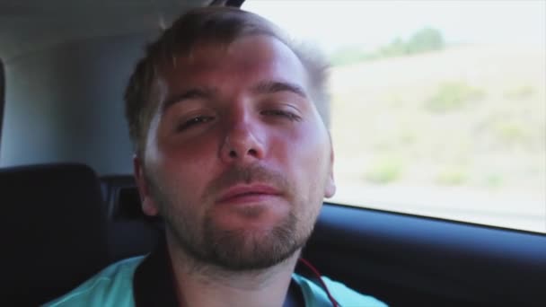 Jeune homme barbu montrer la langue dans la caméra avec les yeux fermés à l'intérieur de la voiture de conduite. Du vent. Fenêtre ouverte
. - Séquence, vidéo