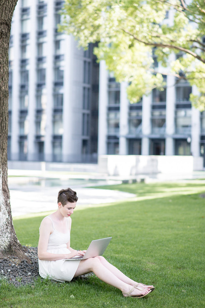 Young woman using tablet outdoor sitting on grass, smiling. - Фото, изображение