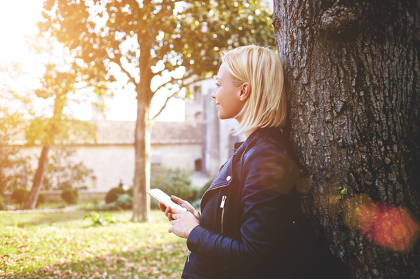  Улыбающаяся женщина с мобильным телефоном в руках мечтает о чем-то хорошем во время отдыха на природе
 - Фото, изображение