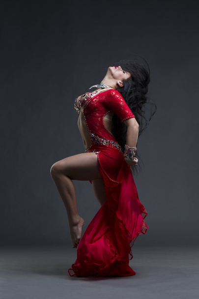 Young beautiful exotic eastern women performs belly dance in ethnic red dress on gray background - 写真・画像