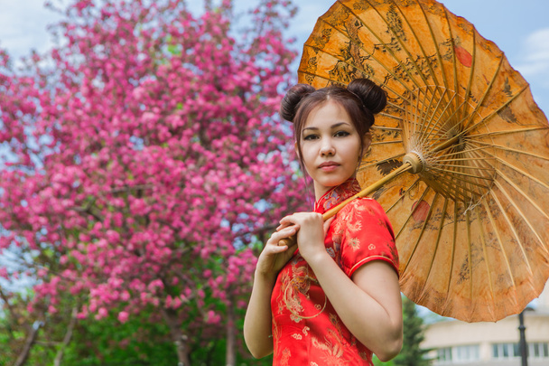 Beautiful asian girl in traditional chinese red dress with bamboo umbrella. - Фото, изображение