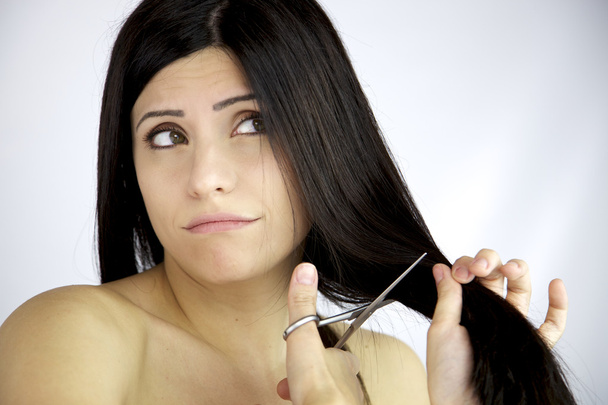 Modelo feminino bonito duvidoso sobre o corte de seu cabelo preto longo
 - Foto, Imagem