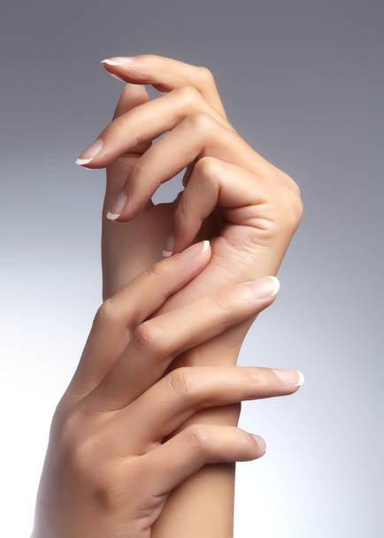Beautiful female arms with ideal french manicure on grey background. Care about female hands, healthy soft skin. Spa & cosmetics. Beauty care. Close-up of beautiful famele fingers with nails polish - Fotó, kép