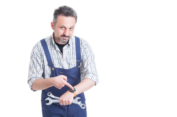 attraktiver junger Reparateur zeigt mit dem Finger auf seine Uhr - Foto, Bild