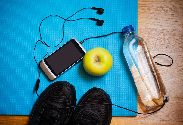 Sportgeräte. Turnschuhe, Wasser, Apfel, Smartphone und Kopfhörer auf Yogamatte - Foto, Bild