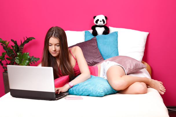 Brunette teenager using a laptop in her room - Photo, Image
