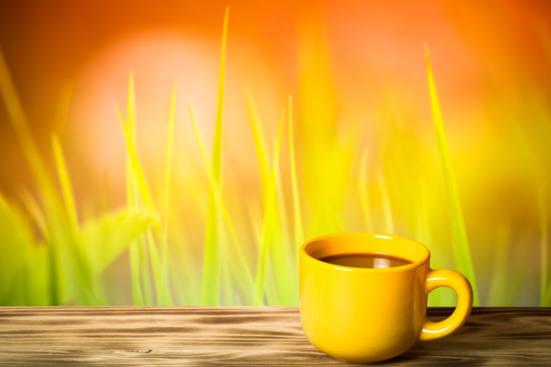 Coffee in yellow cup on wooden table opposite a defocused natura - Photo, Image